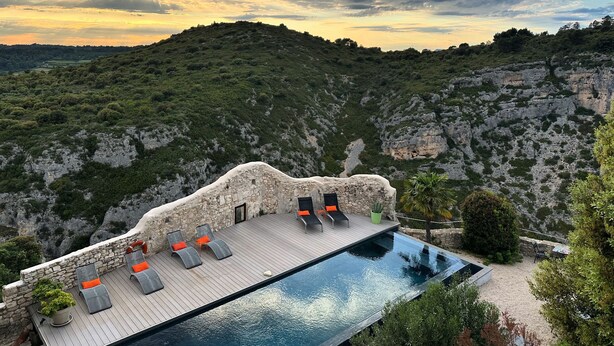 A rooftop infinity pool with lounge chairs and a stone wall. - Metafort (Méthamis)