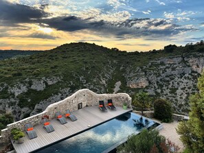 A rooftop infinity pool with lounge chairs and a stone wall.