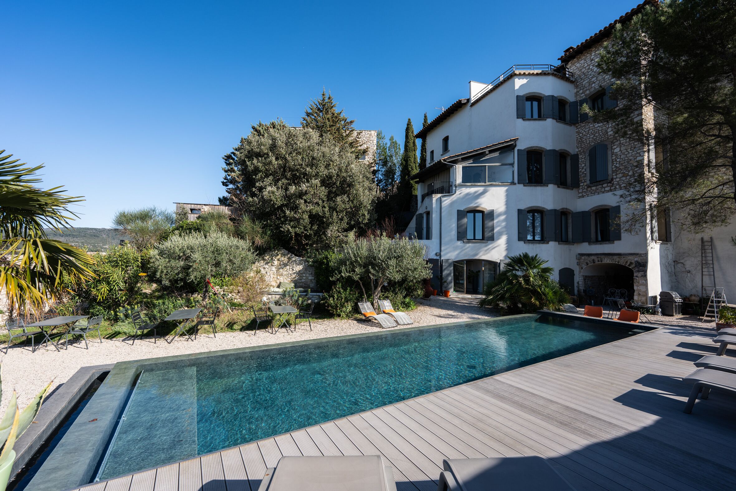 A pool area with a wooden deck, lounge chairs, and a clear blue pool.