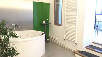 A modern bathroom with a large bathtub, a green accent wall, a small window, and a radiator.