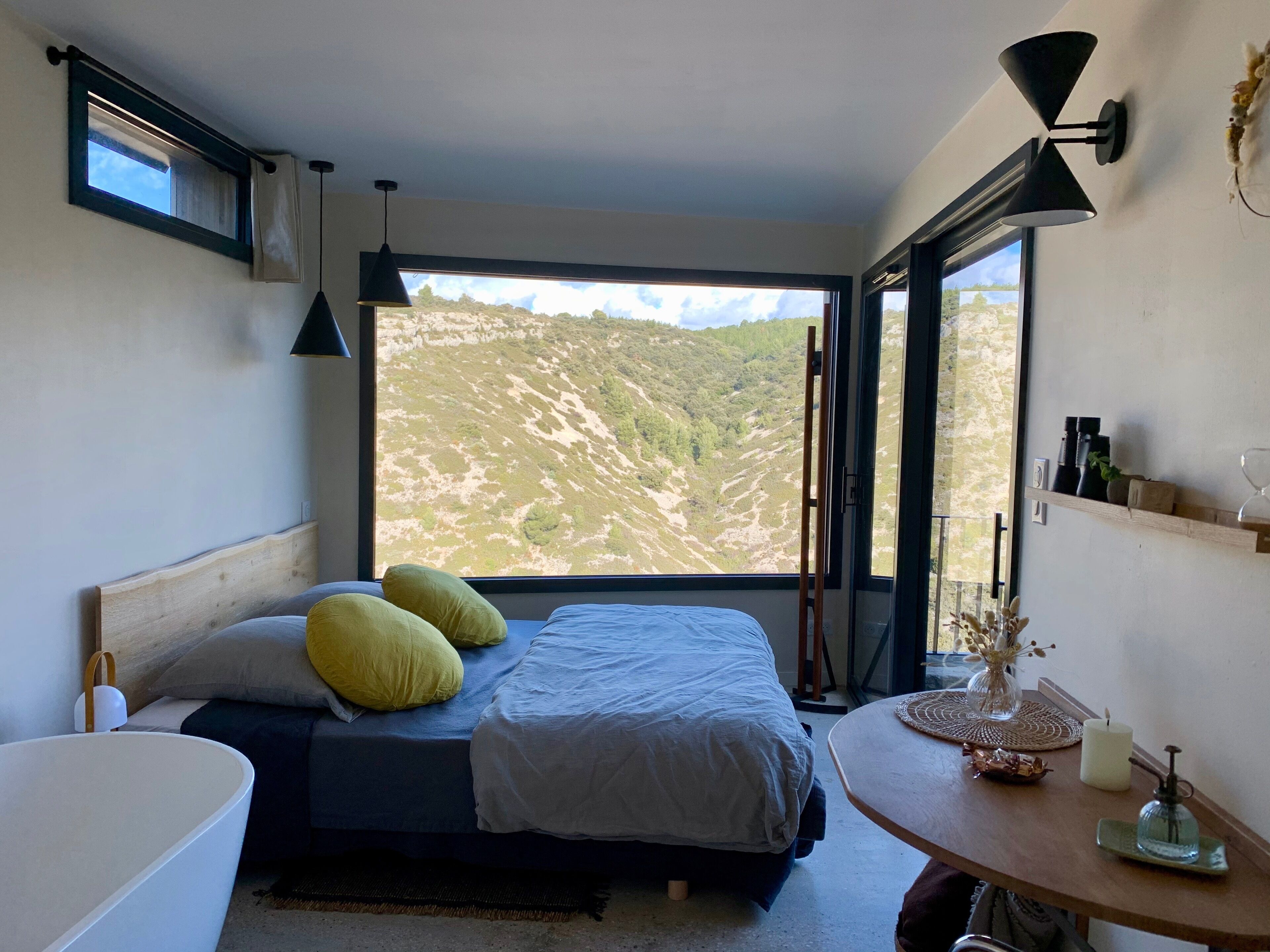 Une chambre à coucher comprenant un lit, une table de chevet, une fenêtre donnant sur un paysage montagneux et une lampe fixée au mur.