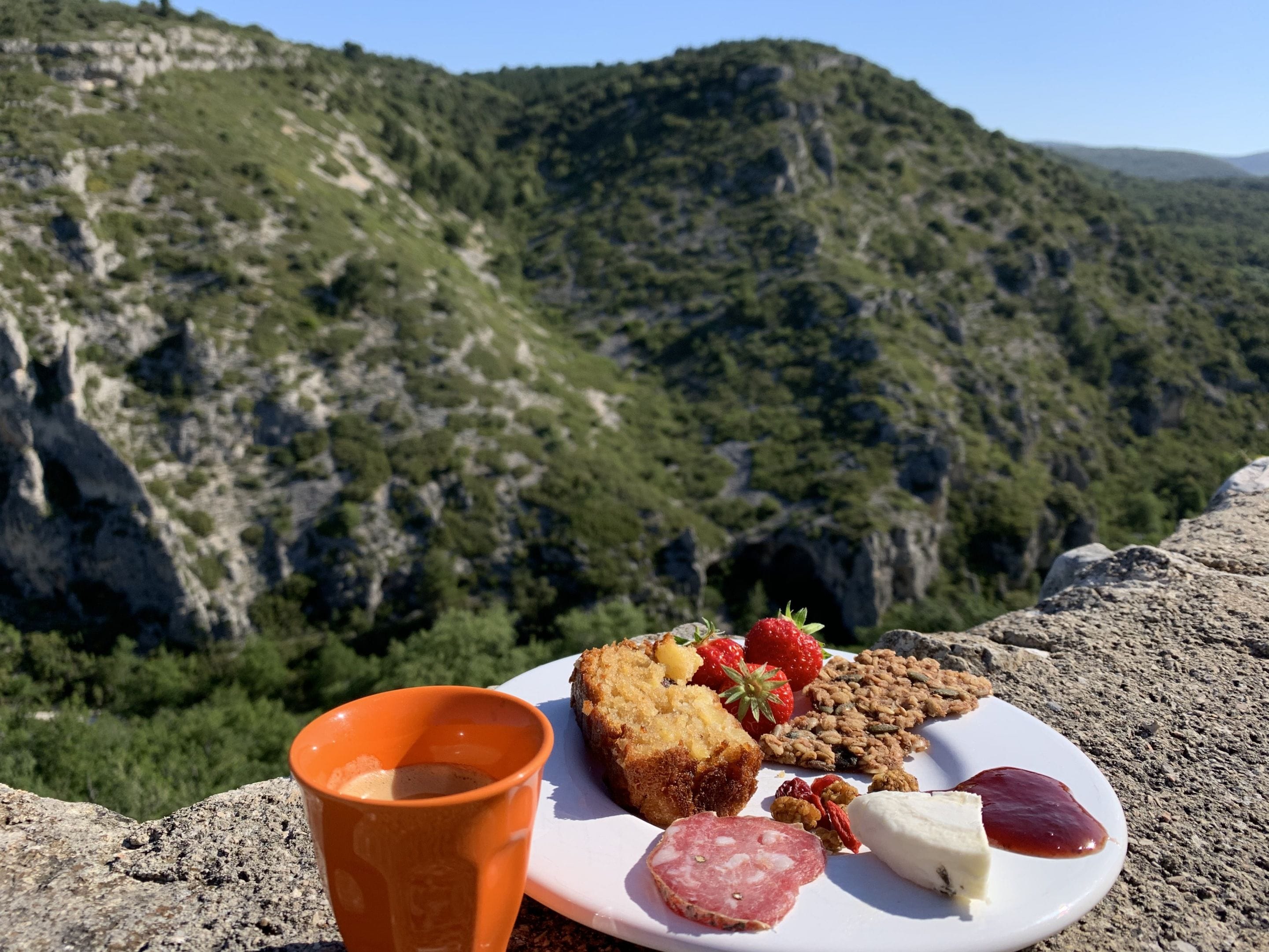 A plate with food items and a cup on a rocky surface with a mountainous backdrop.