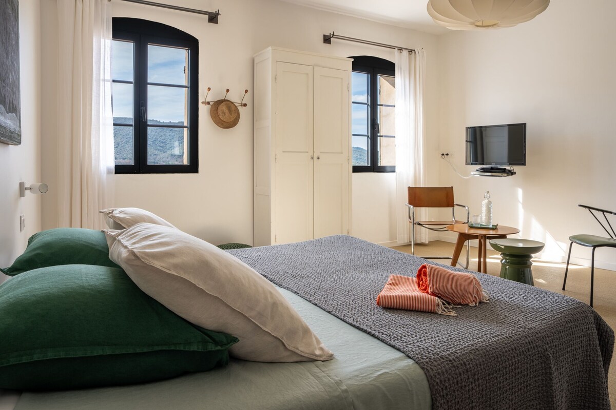 A hotel room with a bed, a TV, a chair, and a desk.