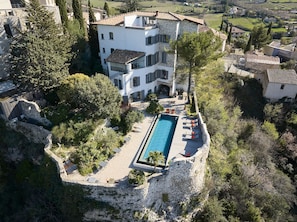 A multi-story building with a swimming pool surrounded by stone walls and vegetation. - Metafort (Méthamis)