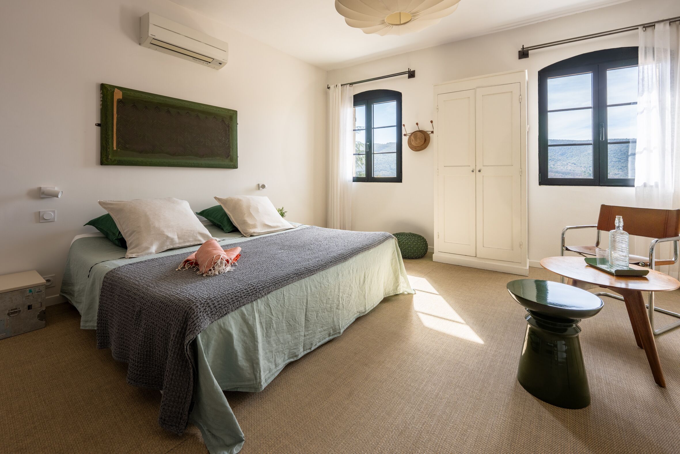 Un dormitorio con cama, mesita de noche, silla, ventana y puerta.