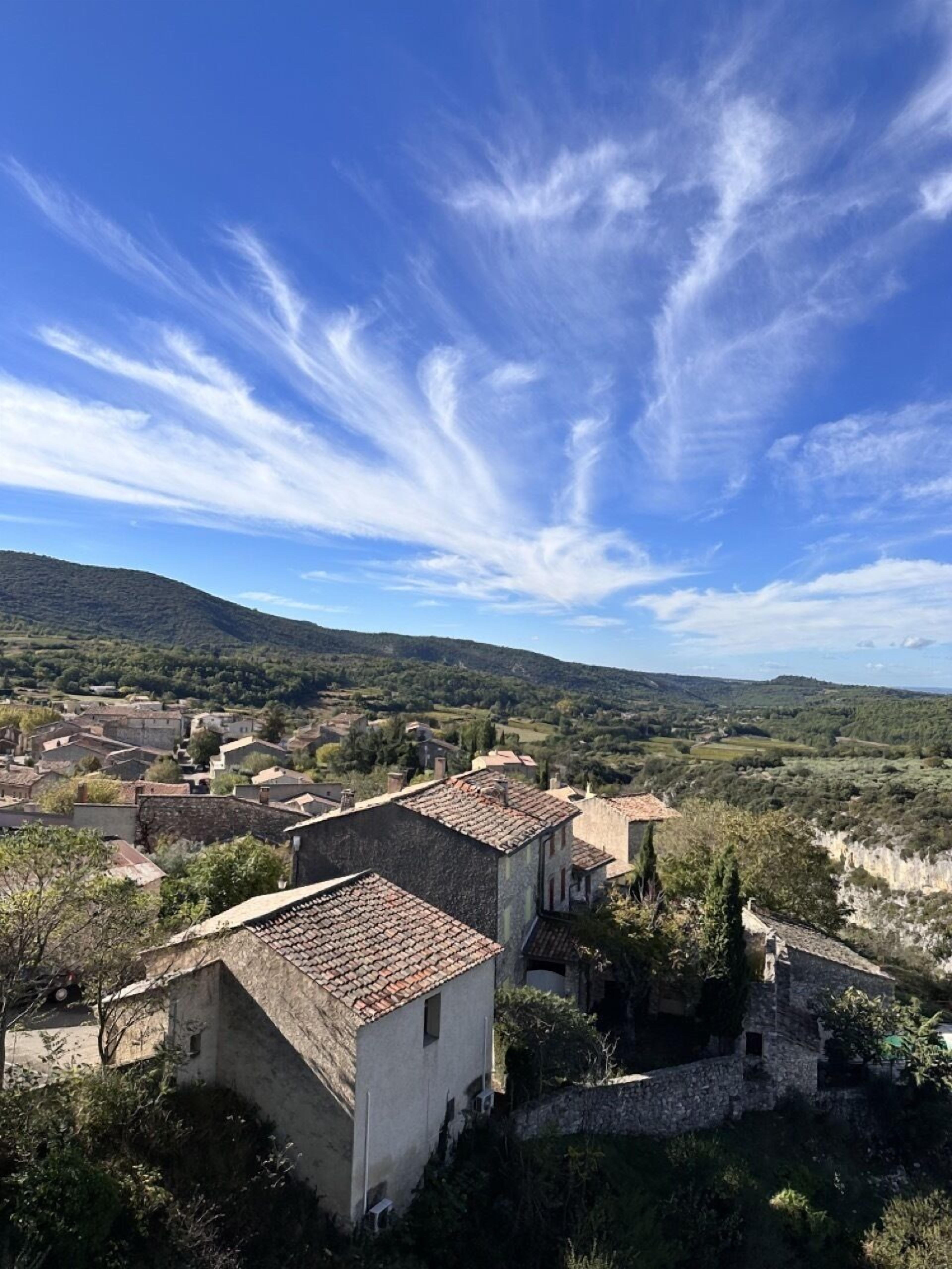 A rural village with traditional stone buildings and terracotta roofs, surrounded by lush greenery and rolling hills.