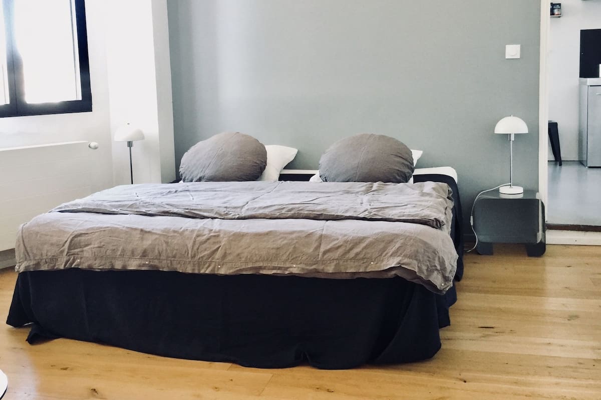 Um quarto com uma cama, mesa de cabeceira, abajur e janela.