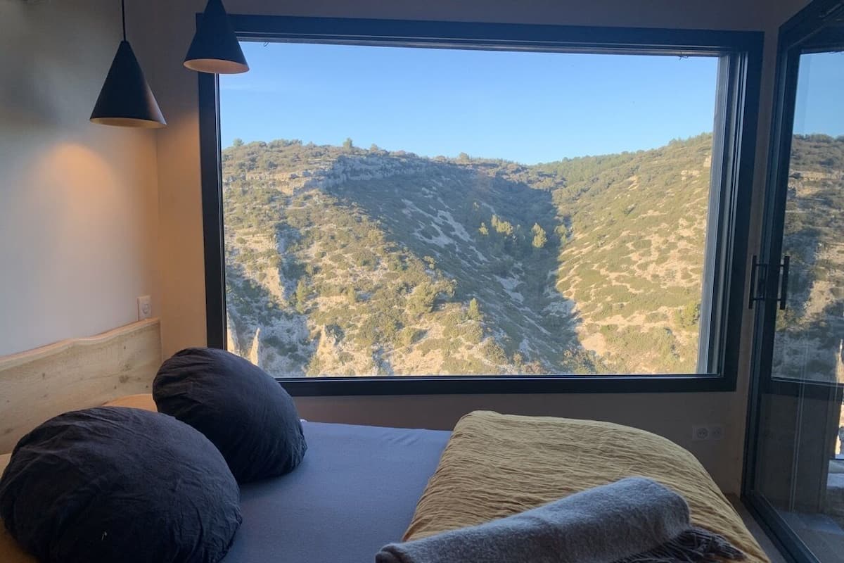 Quarto com uma janela ampla que oferece vista para uma paisagem montanhosa.