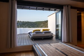 Un balcón con cama, vistas a un paisaje montañoso y una puerta de cristal que da a una habitación.