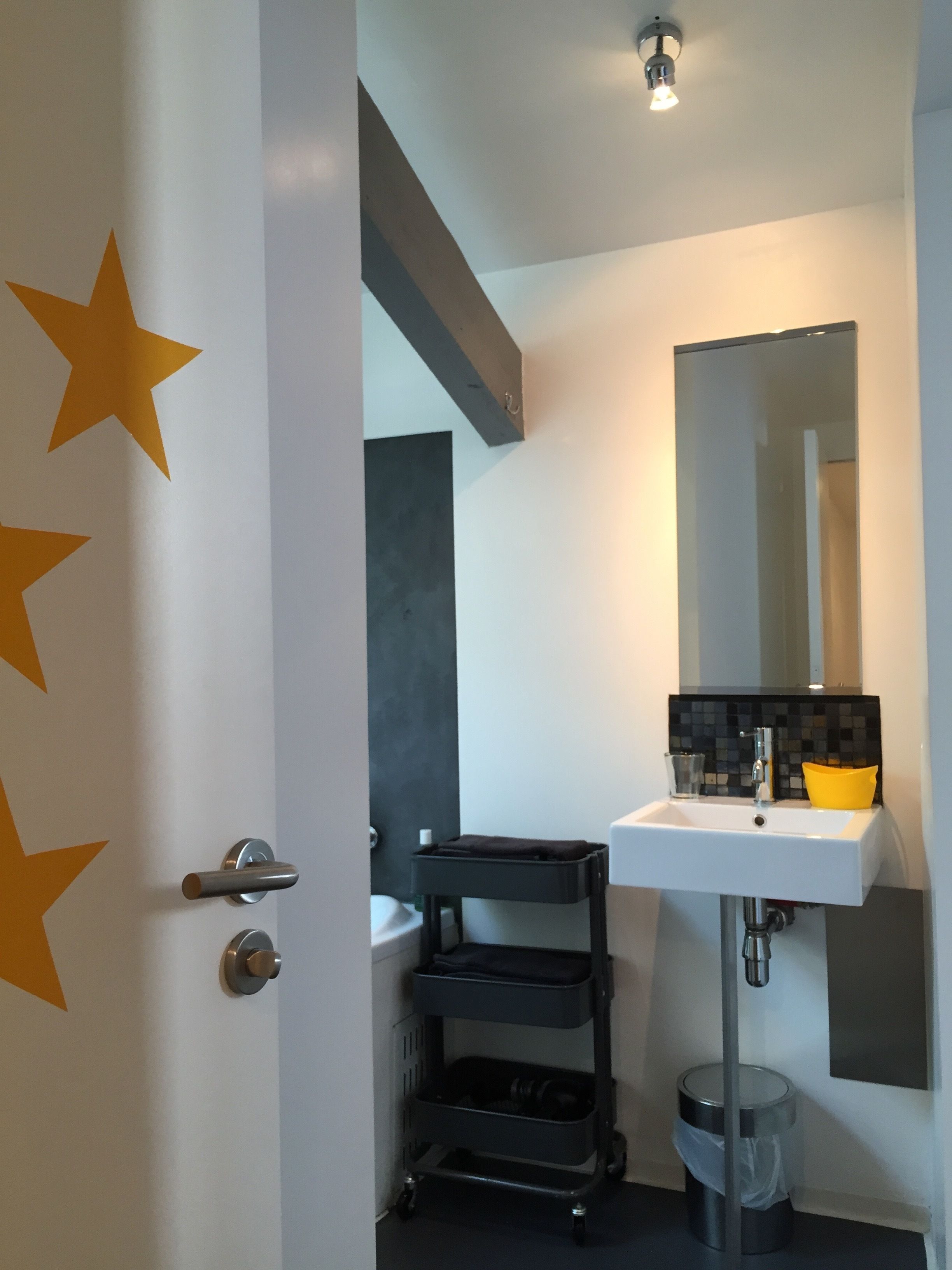 A modern bathroom with a white sink, a mirror, and a black storage cart.