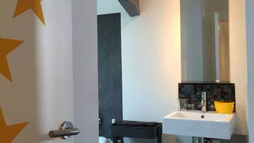 A modern bathroom with a white sink, a mirror, and a black storage cart.