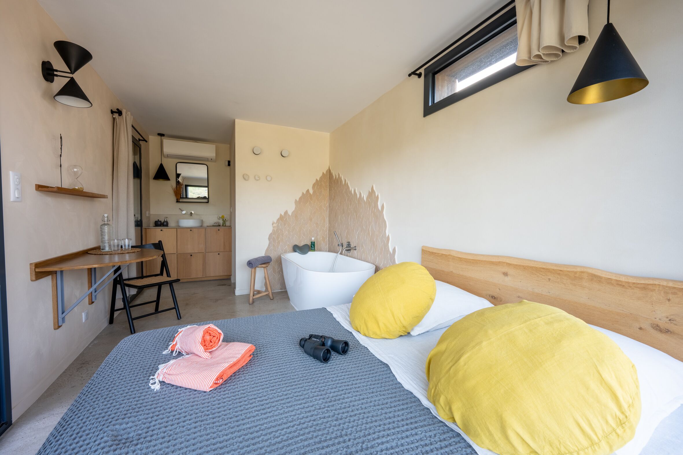 A bedroom with a bed, a desk, a chair, a bathroom with a bathtub, and a window.