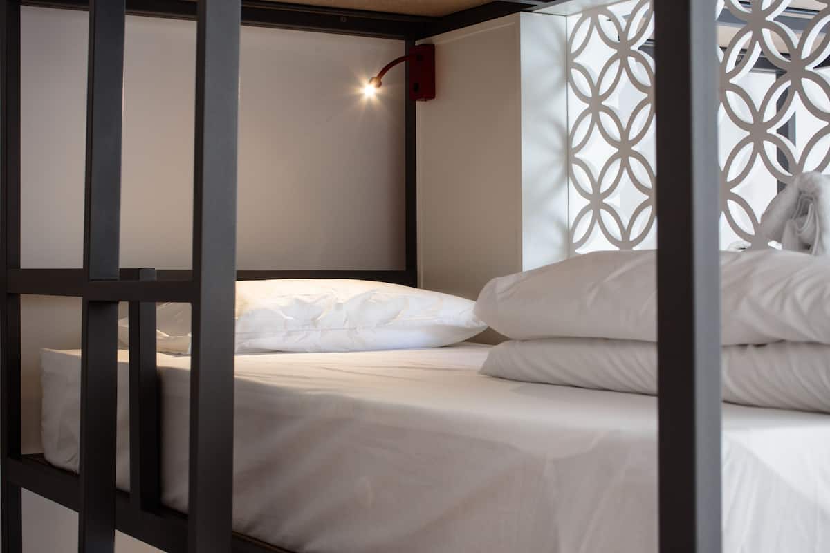 Una litera con ropa de cama blanca y una lámpara roja.