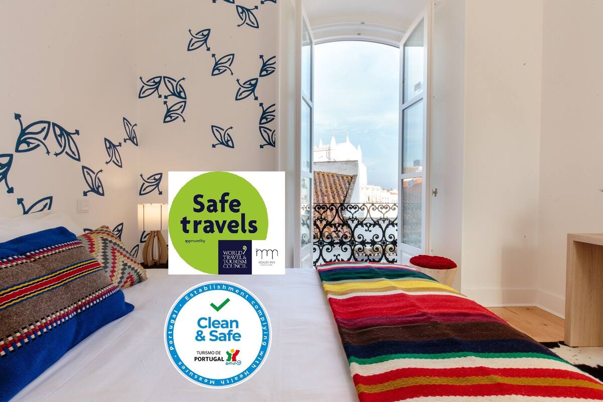 Habitación de hotel con cama, vista de un edificio a través de una puerta abierta y calcomanías que indican seguridad e higiene.