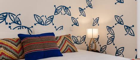 A bed with patterned pillows, a bedside lamp, and a wall with a leaf pattern.