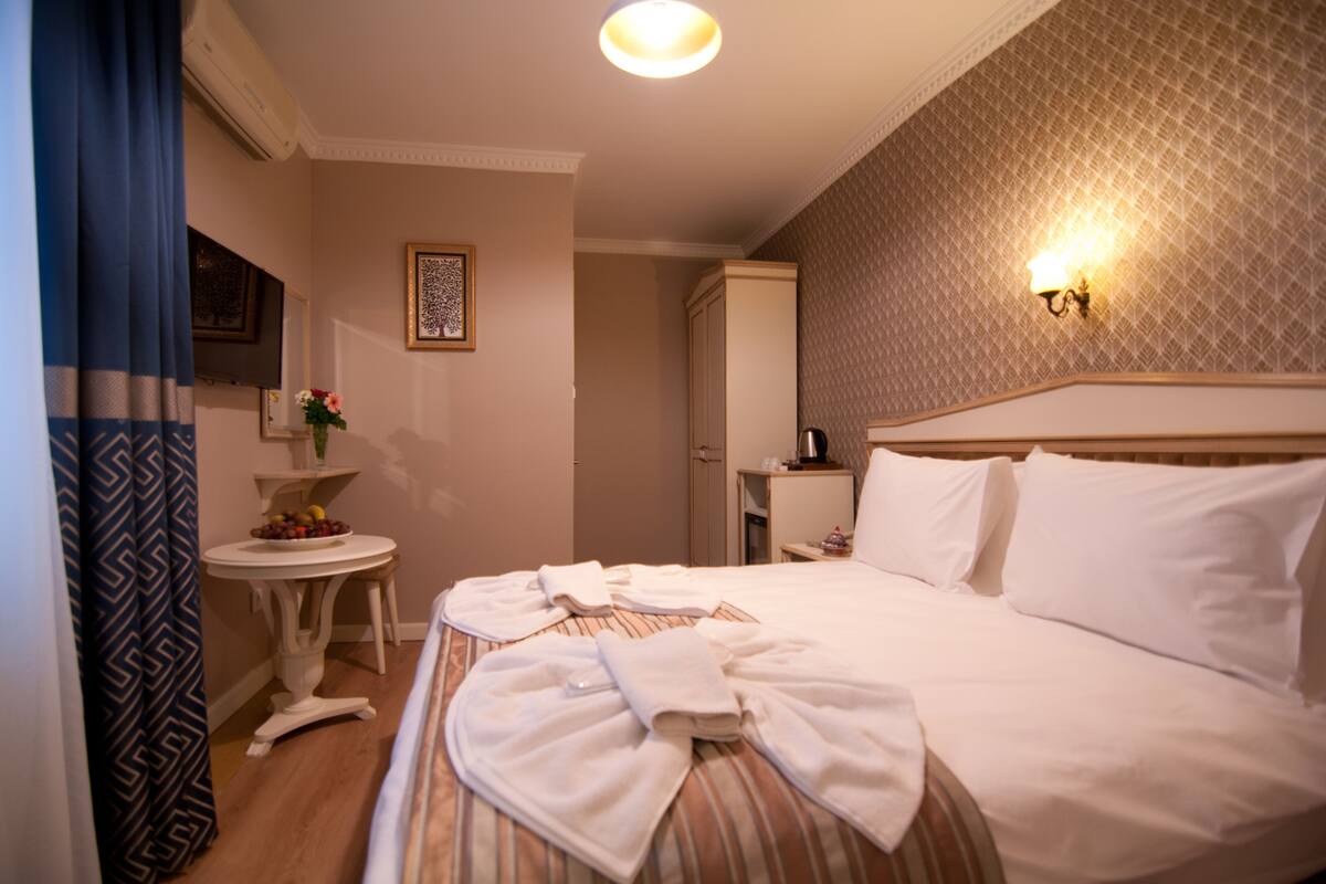 A hotel room with a large bed, a small table with a vase of flowers, a wall-mounted light fixture, and a patterned wall.