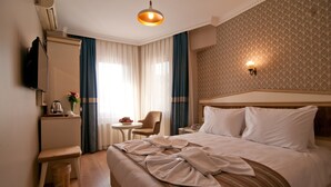 A hotel room with a large bed, a desk with a chair, a small table with a lamp, and a television on the wall. - Mevlana Hotel (Istanbul)