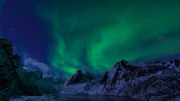 Paisaje montañoso nevado con un lago tranquilo y auroras boreales.