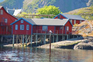 A red wooden house with a blue roof, situated on stilts over water.