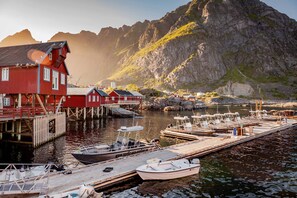 En hamn med förtöjda båtar, en röd byggnad och ett bergigt landskap i bakgrunden.