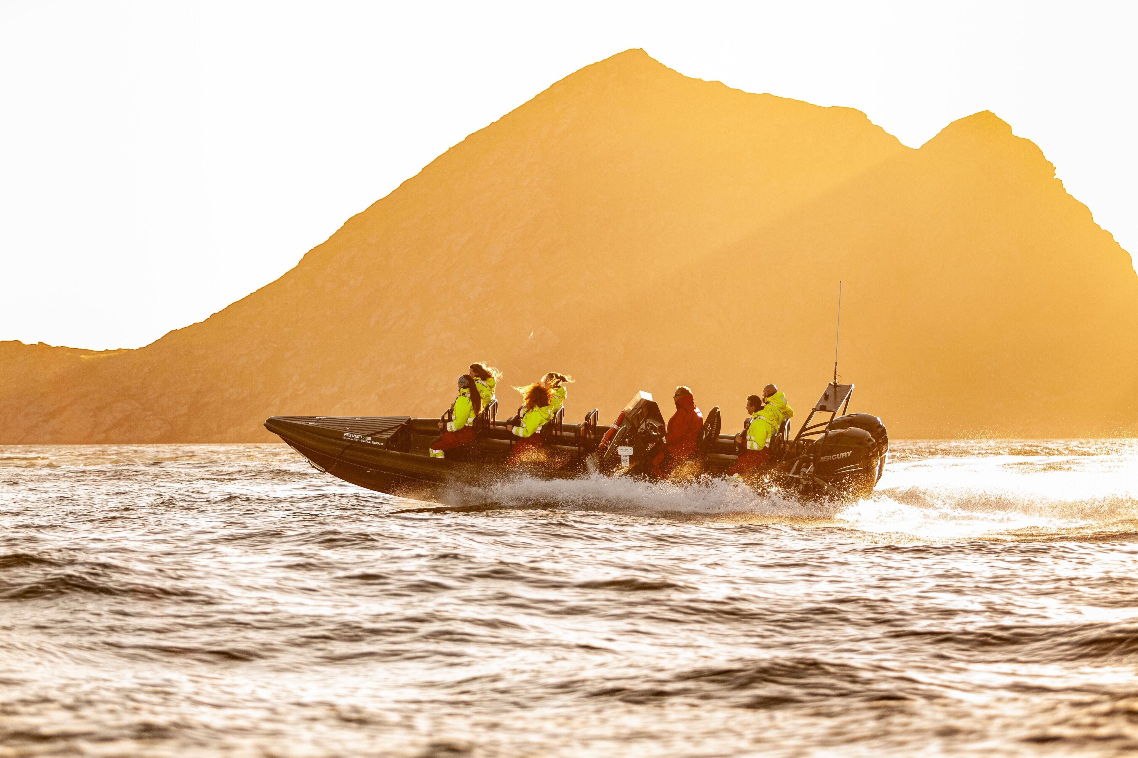 A speedboat with passengers on a body of water with a mountain in the background.