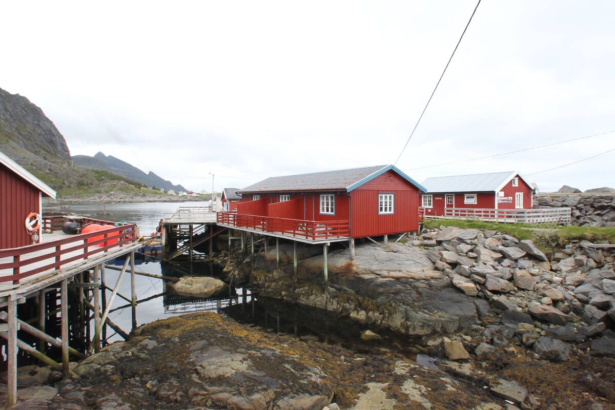 A red wooden building with a dock extending into the water, surrounded by rocky terrain and mountains in the background.