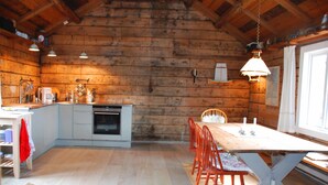 A rustic wooden cabin interior with a kitchen, dining area, and a large window.