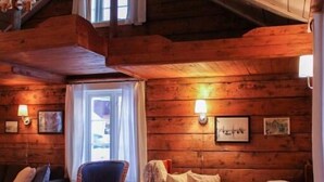 A cozy log cabin interior with a wooden ceiling, a sofa, a chair, and a table with a candle.