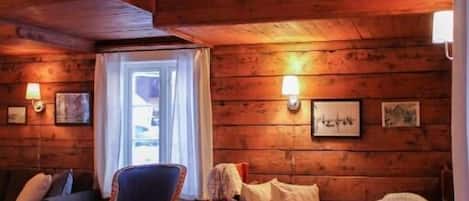 Interior acogedor de una cabaña de madera con techo de madera, un sofá, una silla y una mesa con una vela.