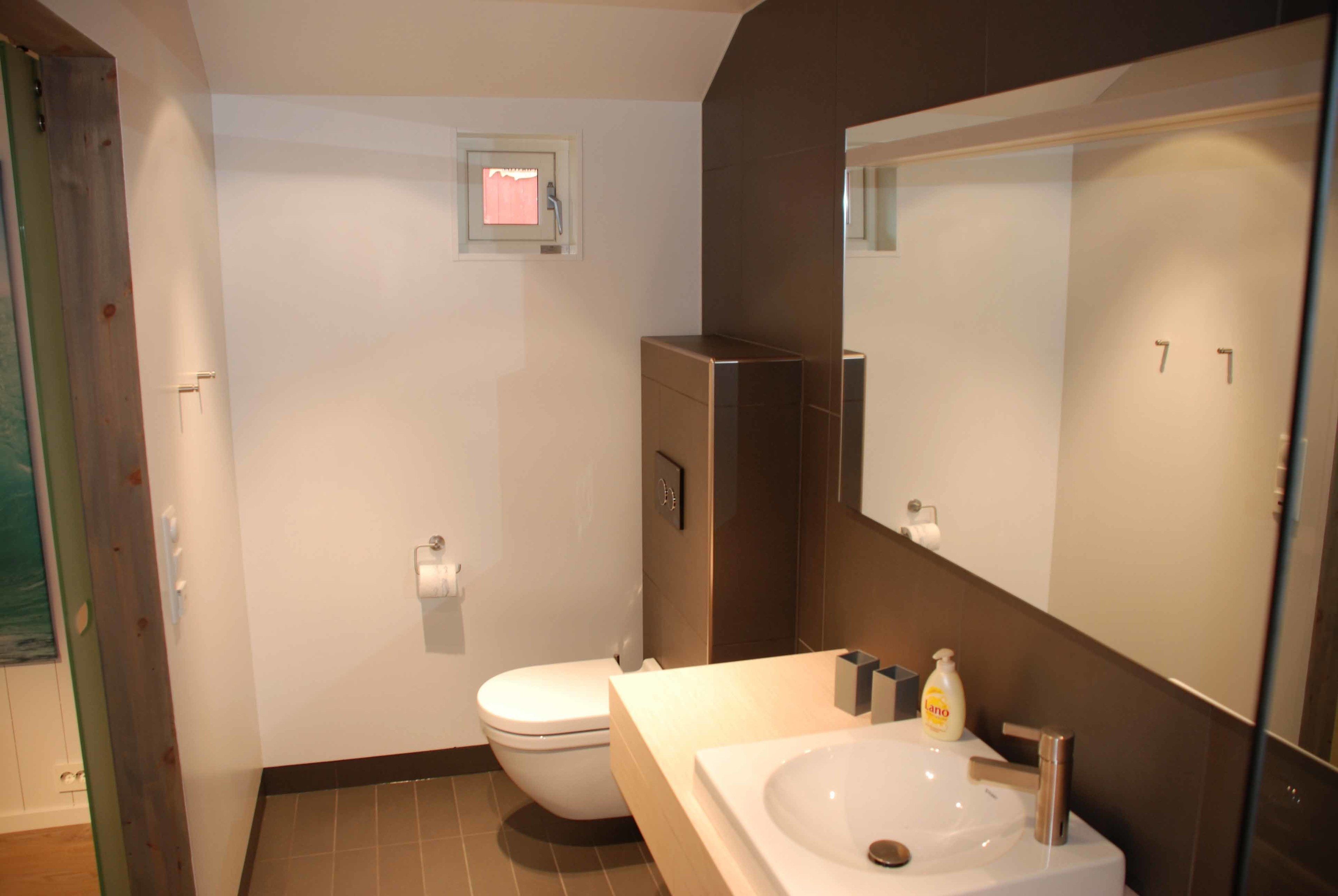 Et moderne badeværelse med toilet, stort spejl og håndvask.