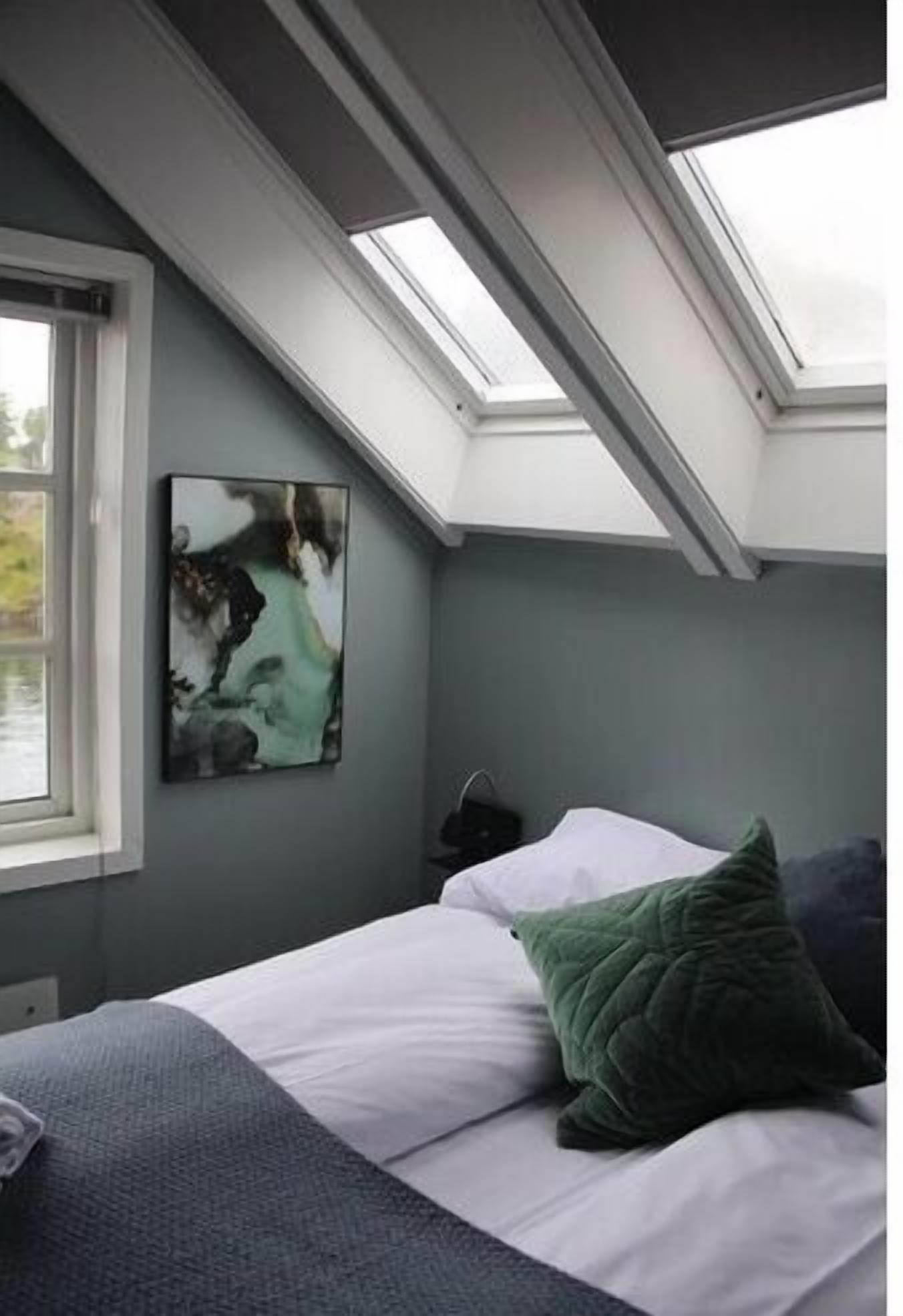 Une chambre avec une lucarne, un lit avec des oreillers et un tableau accroché au mur.