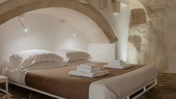 A bedroom with a stone floor, a bed with white linens, and a stone wall.