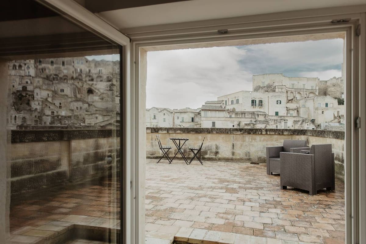 A view from a balcony with a table and chairs, overlooking a historic town with white buildings and a stone wall.