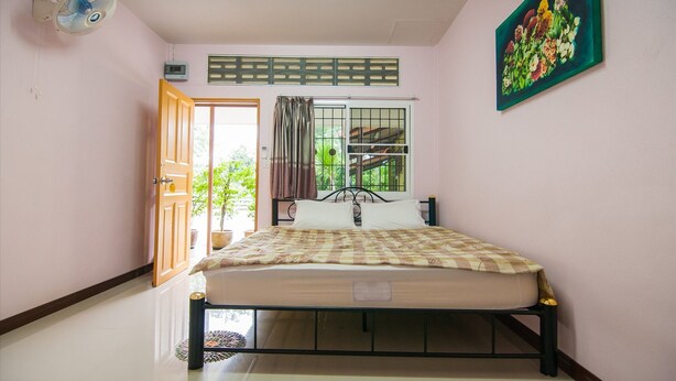 A bedroom with a bed, a window with a view, a fan, and a painting on the wall. - Bansabai Raiwan Resort (Chanthaburi)