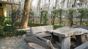 A rustic outdoor seating area with wooden benches and a table, surrounded by trees and a fence. - Bansabai Raiwan Resort (Chanthaburi)