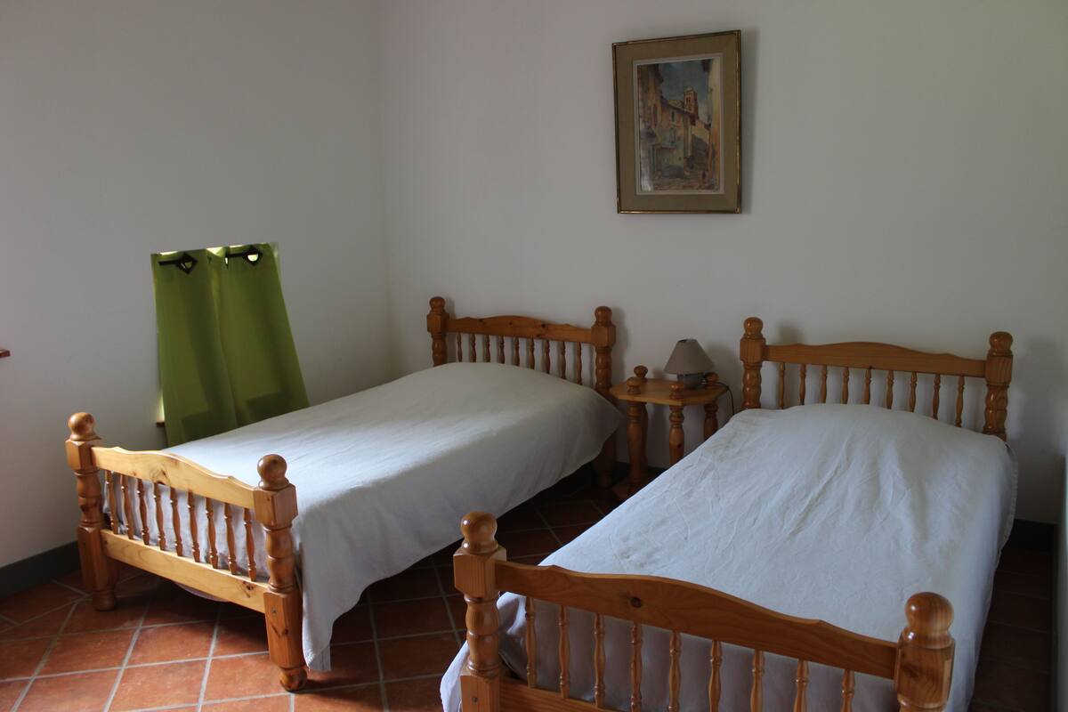 Two wooden beds with white linens in a room with tiled flooring and a painting on the wall.