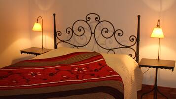 Een netjes opgemaakt bed met een rood-witte deken, twee bedlampjes en een houten vloer.