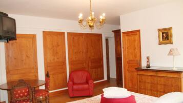 A hotel room with wooden wardrobes, a red armchair, a small round table, and a bed with red and white pillows.