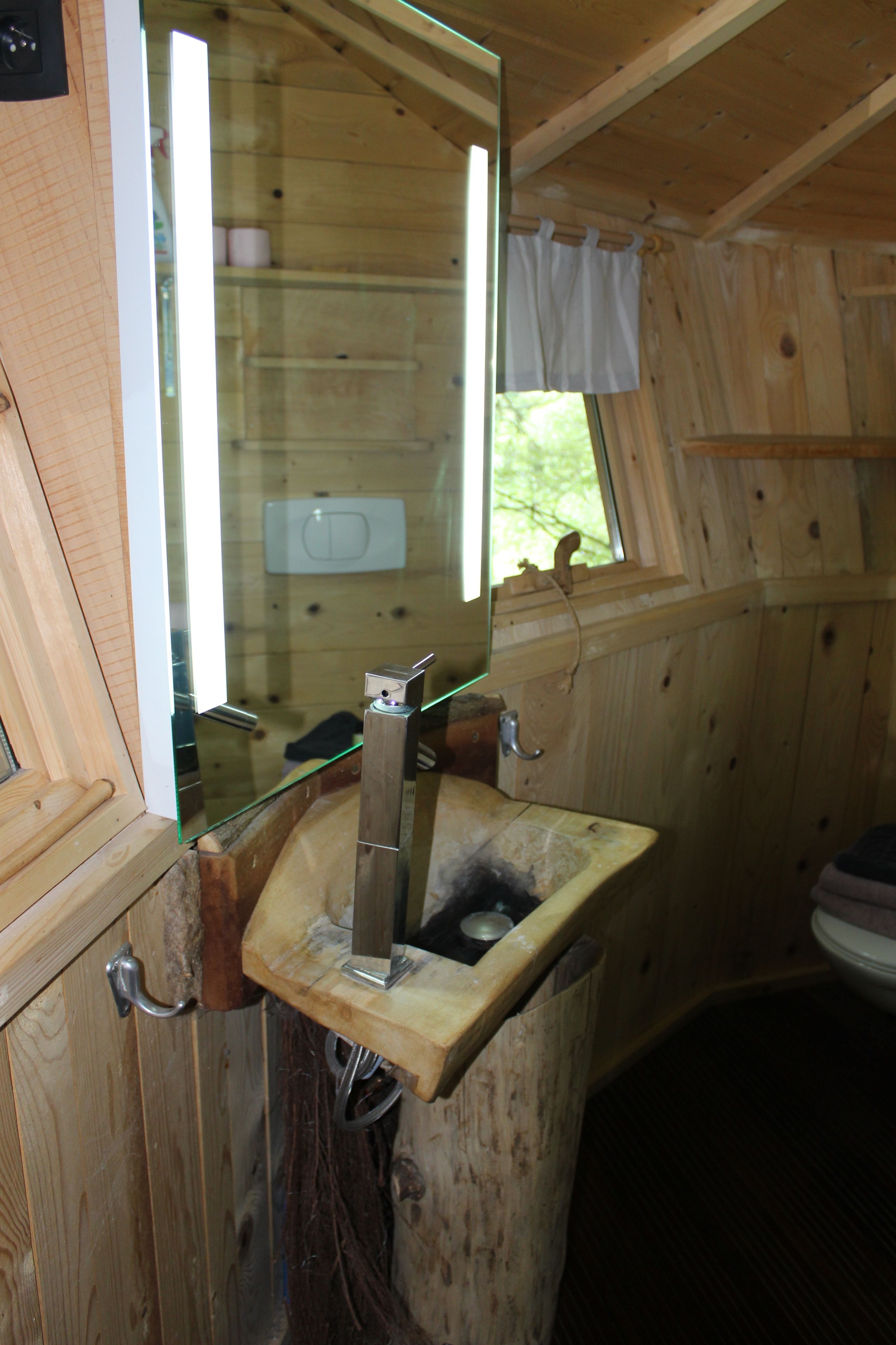 A wooden cabin bathroom with a wooden sink, a window with a curtain, and a toilet.