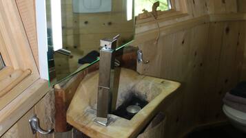 A wooden cabin bathroom with a wooden sink, a window with a curtain, and a toilet.