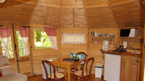 A cozy cabin interior with a wooden dining table, chairs, a small kitchenette, and a bed.