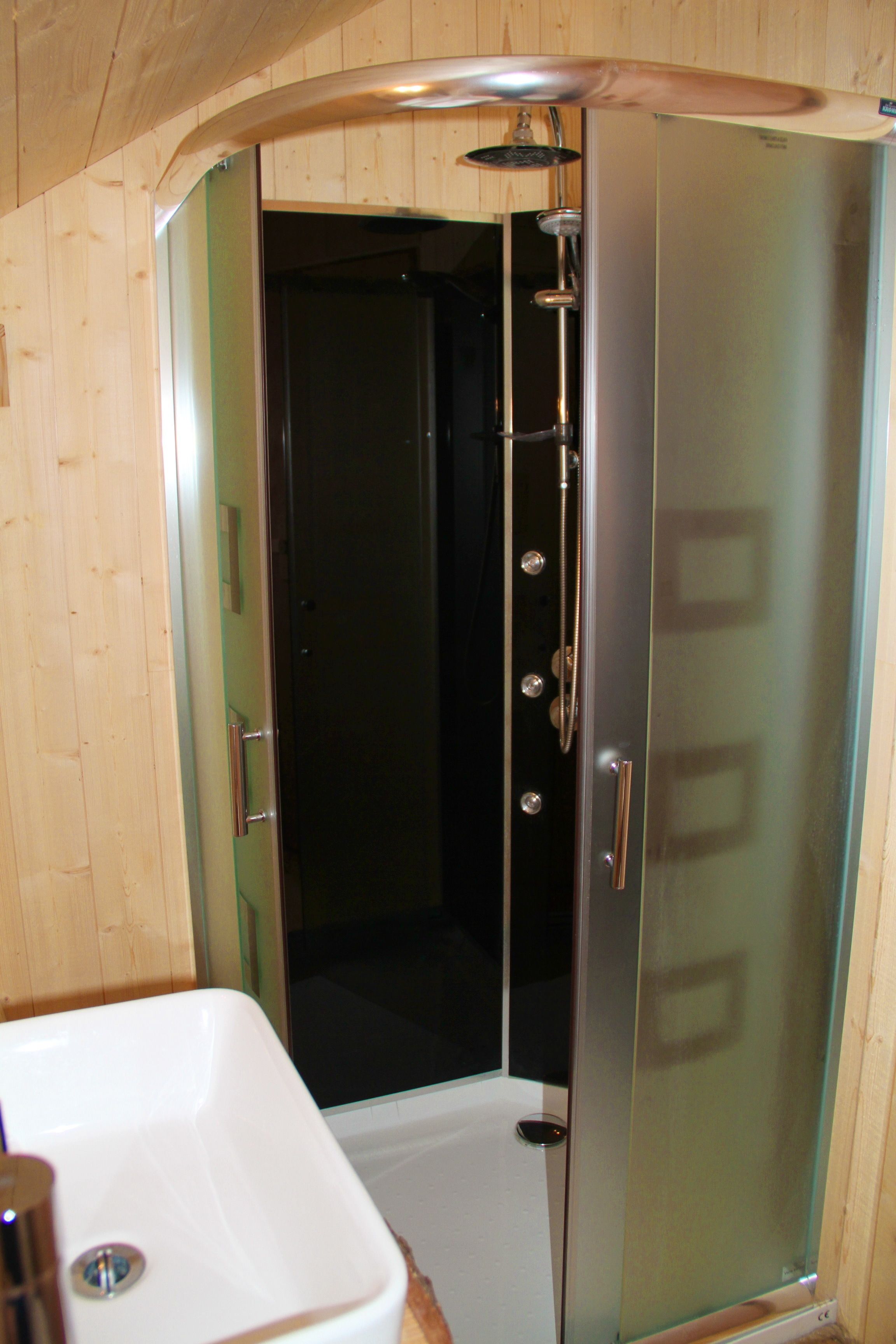 A modern bathroom with a glass shower enclosure, a white sink, and wooden paneling.