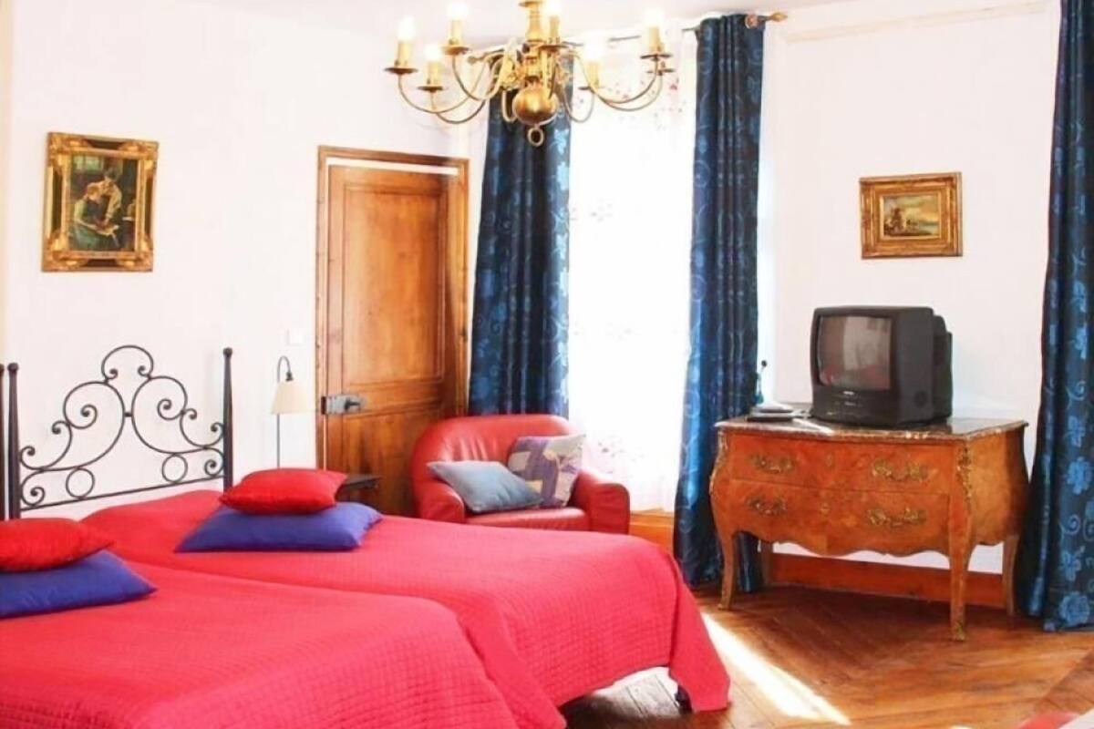 A bedroom with two beds, a wooden dresser, a television, and a chandelier.