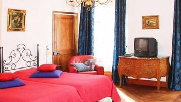 A bedroom with two beds, a wooden dresser, a television, and a chandelier.