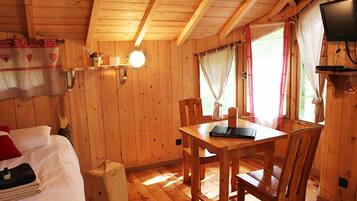 Een houten kamer met een bed, een tafel, stoelen, een televisie en gordijnen.
