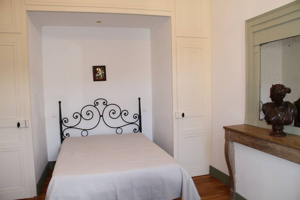 A bedroom with a bed, a wooden dresser, a mirror, and a door.