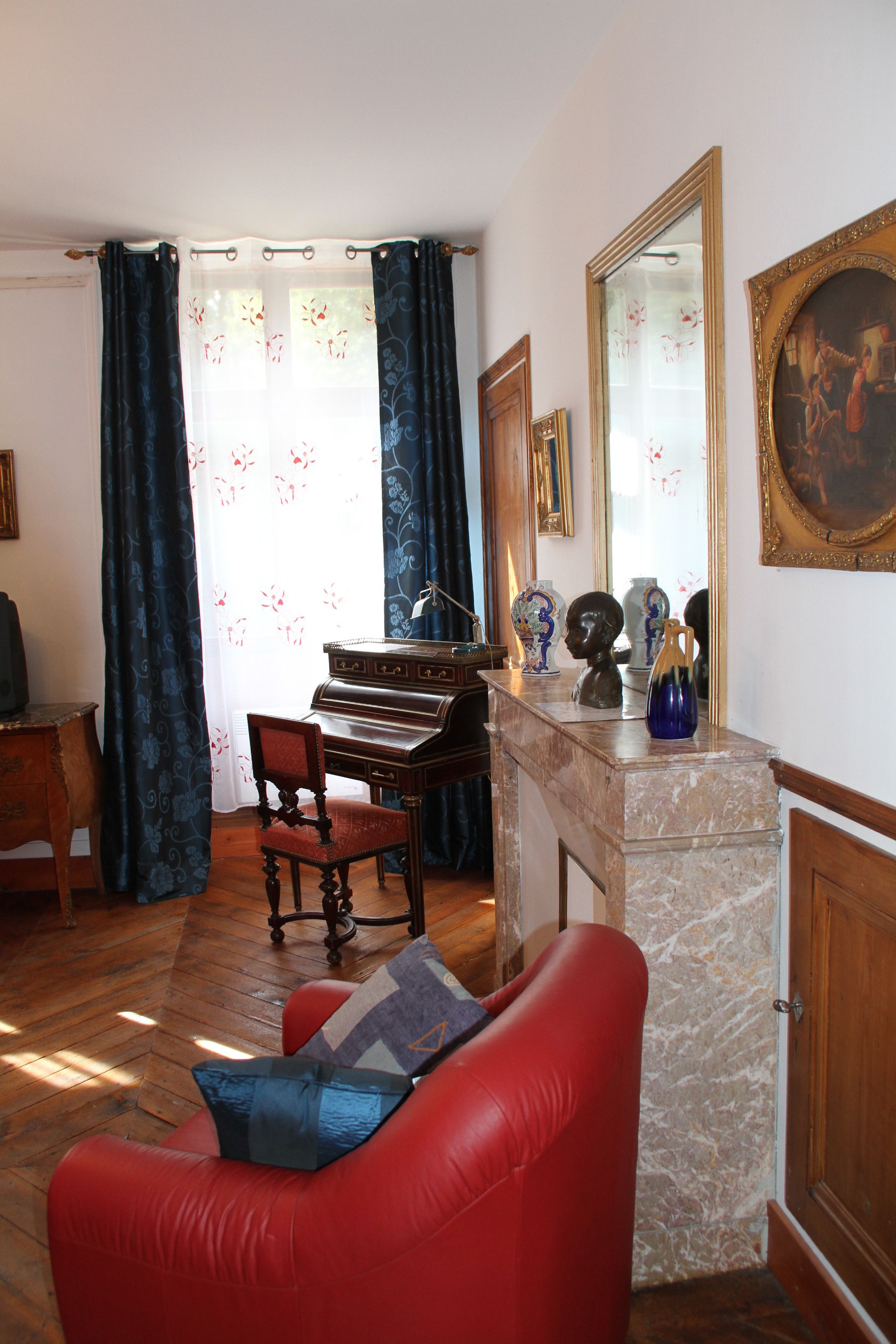 Un salon avec un piano, un fauteuil rouge, un meuble en bois et un grand miroir.