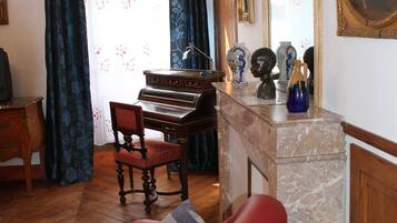 Un salon avec un piano, un fauteuil rouge, un meuble en bois et un grand miroir.