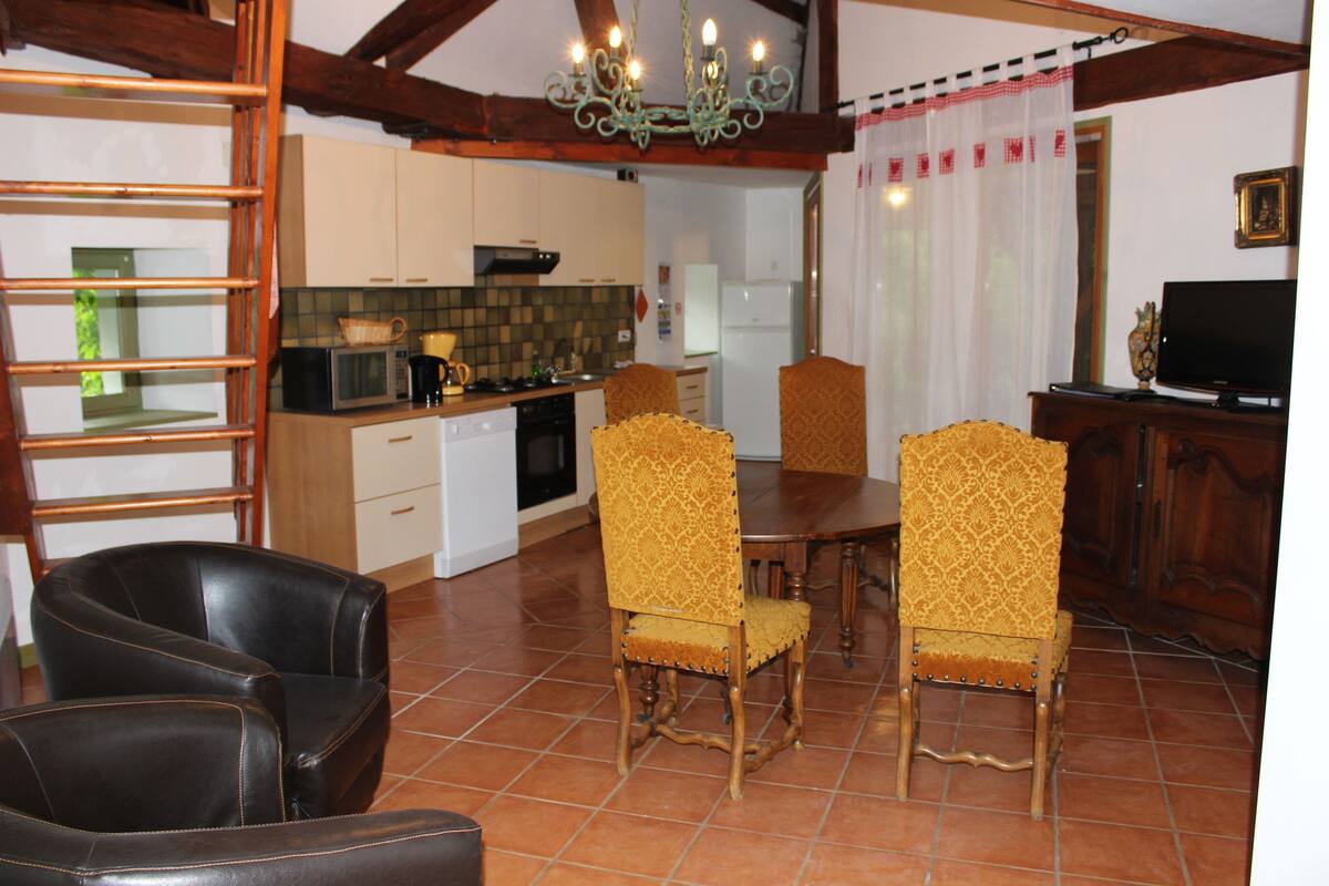 A dining area with a wooden table and four chairs, a kitchen with white cabinets and a microwave, and a television on a wooden cabinet.
