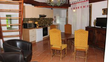 Un coin repas avec une table en bois et quatre chaises, une cuisine avec des meubles blancs et un four à micro-ondes, et un téléviseur posé sur un meuble en bois.